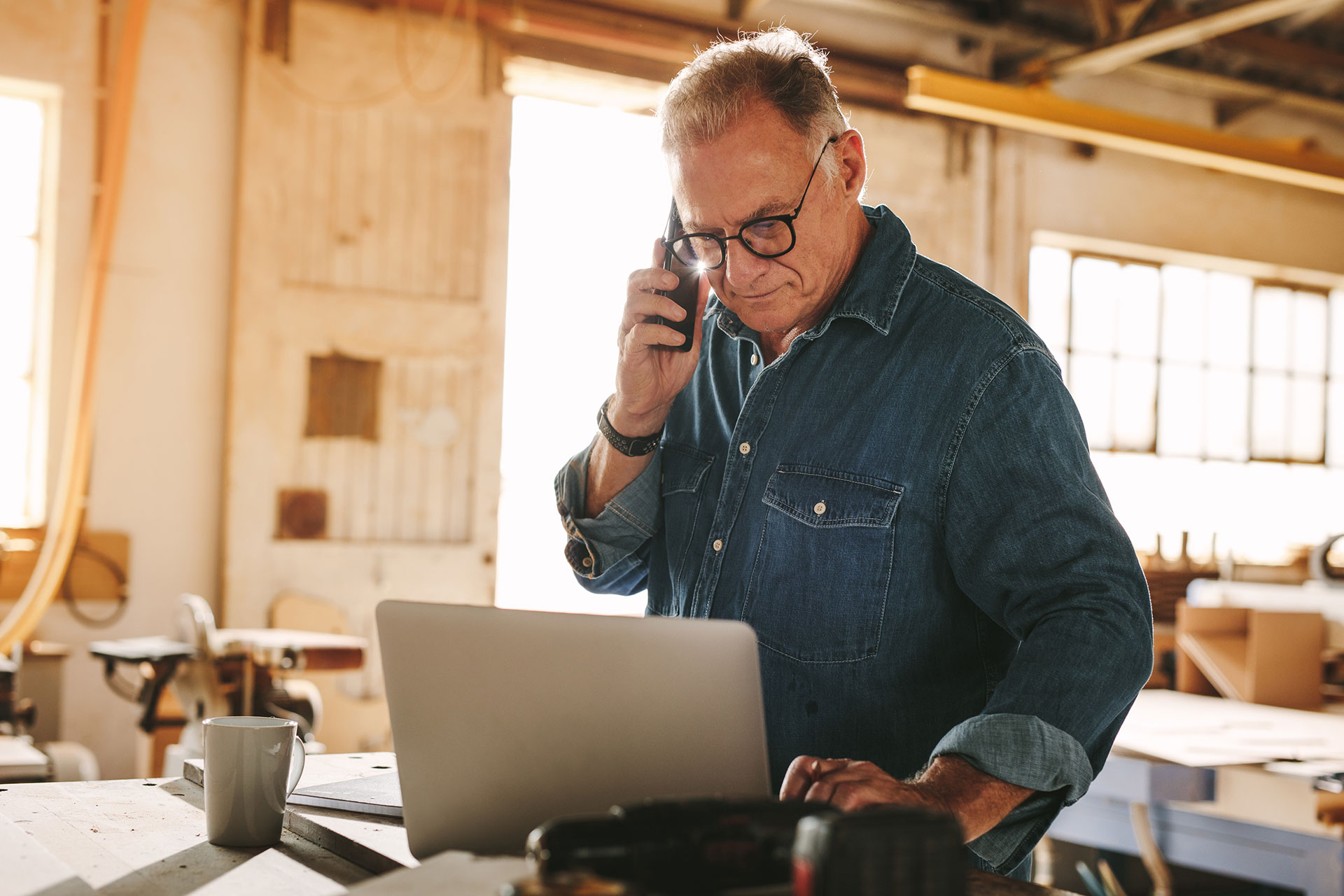 man standing and talking on the phone while looking at his laptop