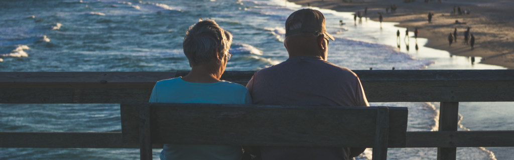 older couple sitting on the bench looking at the water and beach
