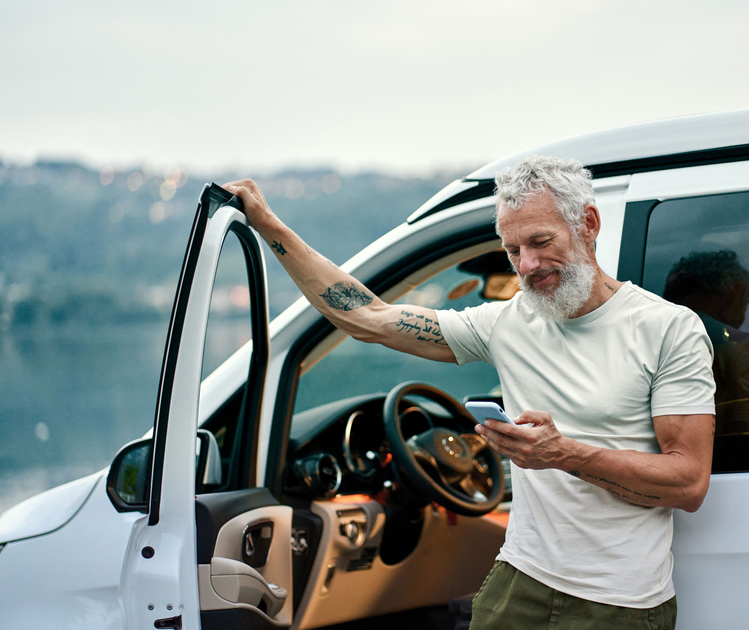 man looking at his phone while leaning on his car