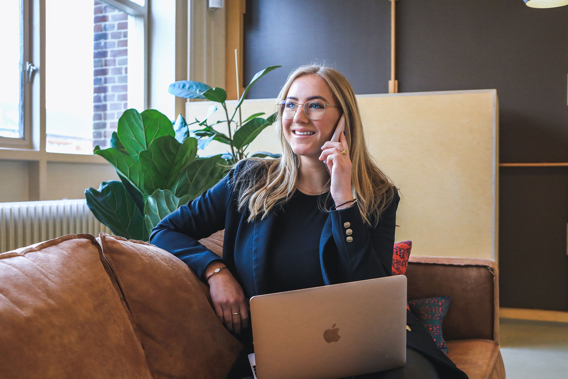woman sitting on her phone smiling with her laptop in her lap