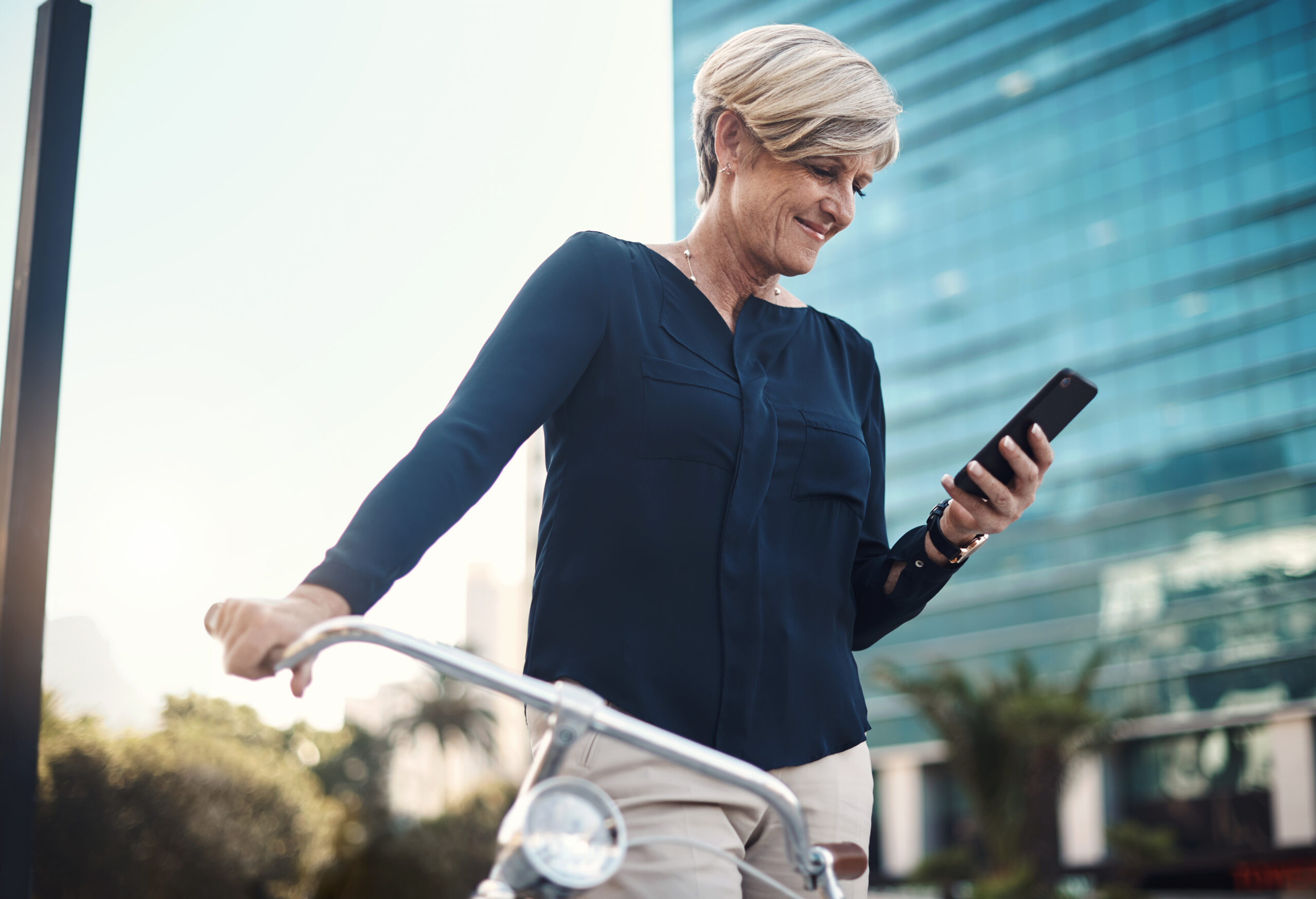 Shot of a mature businesswoman using a smartphone while traveling with a bicycle through the city