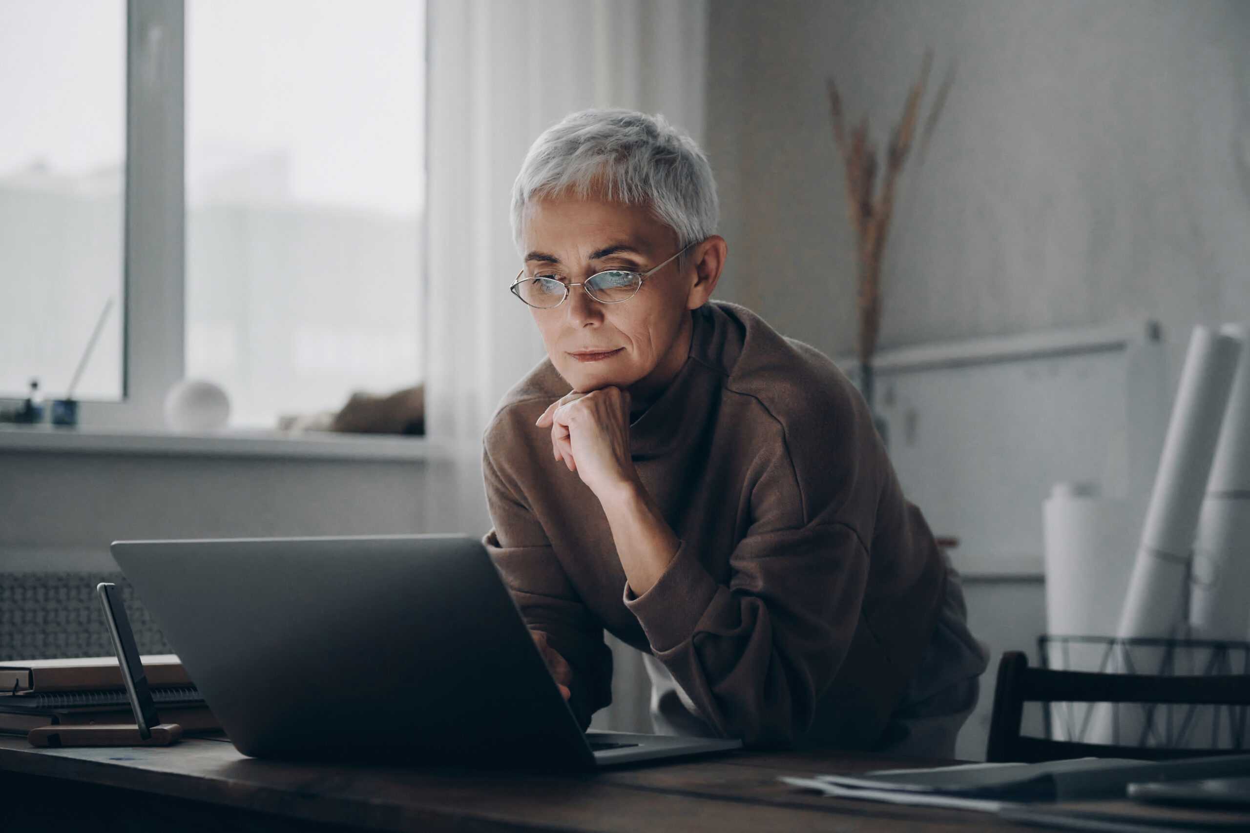 Concentrated senior woman using laptop while working late in office