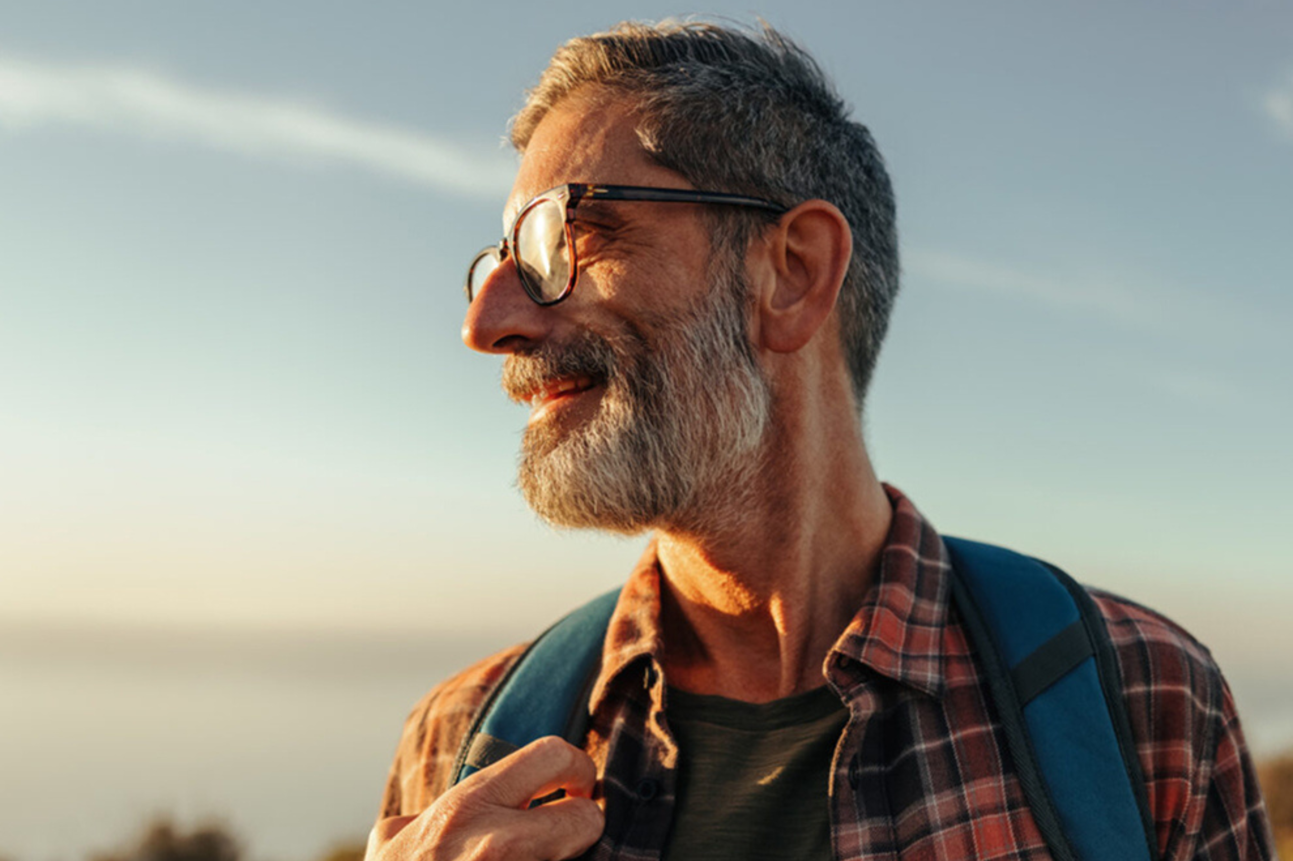 man in glasses looking out into the sun while wearing a backpack outdoors