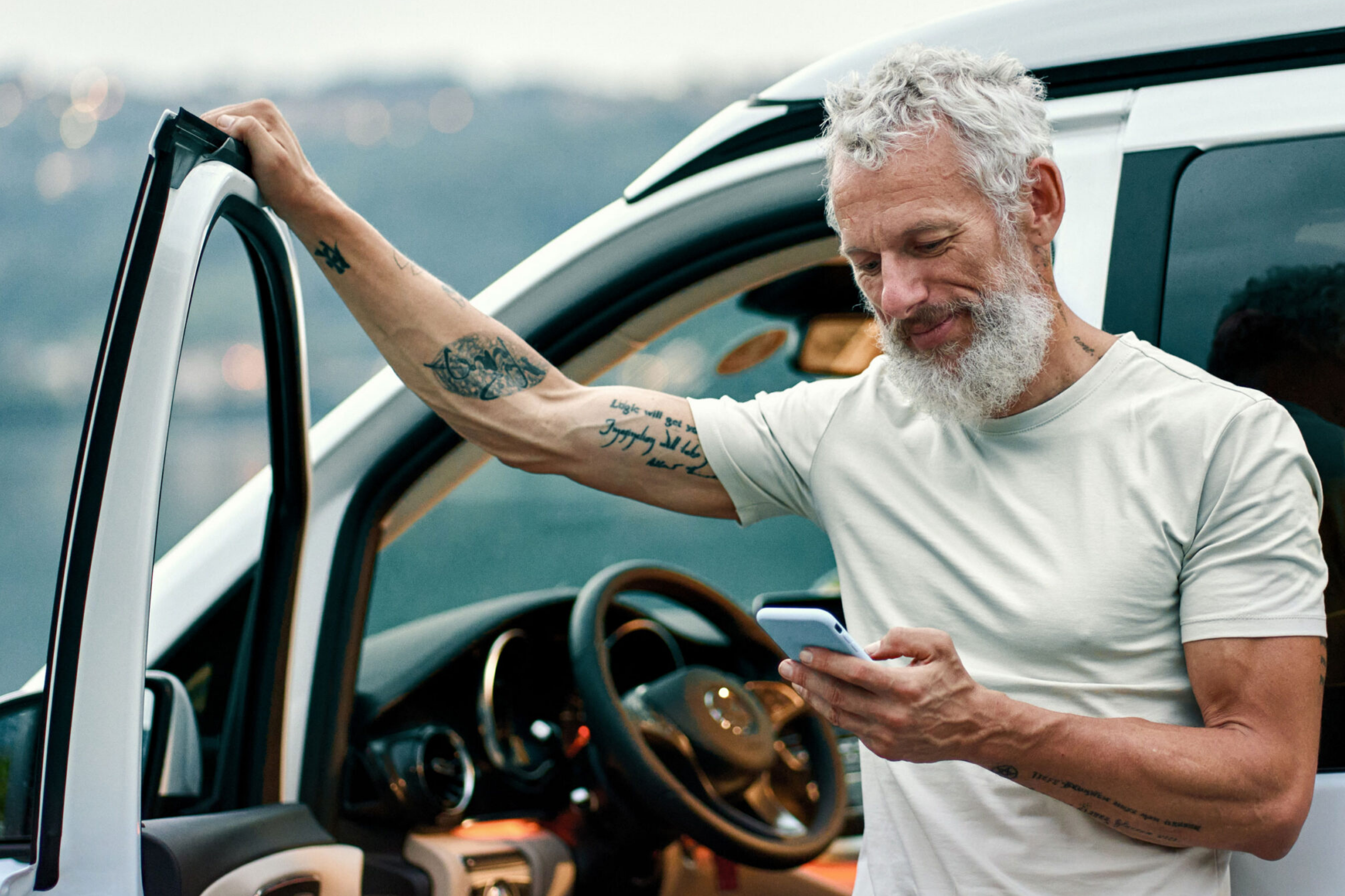 man leaning up against his car door with the door open and looking at his phone